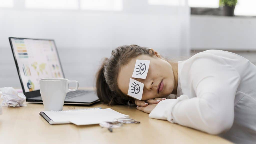 tired businesswoman covering her eyes with drawn eyes paper
