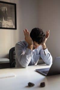 Lack of motivation: Anxious man sat at desk in fron tof laptop, stressed and rubbing his eyes. Image by Freepik.